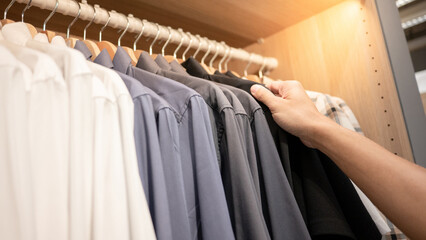 Menswear lifestyle concept. Male hand choosing shirt on hanger hanging in closet or wardrobe.