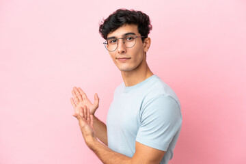 Young Argentinian man isolated on pink background With glasses and presenting something