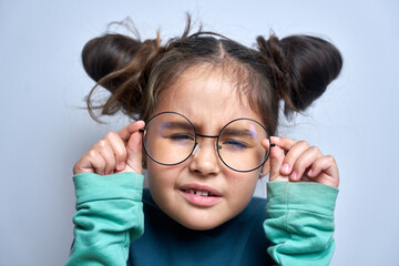 Caucasian little girl wearing glasses squinting while looking at camera isolated on white background. Vision problems concept - obrazy, fototapety, plakaty