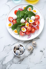 Fresh spinach, cherry tomatoes and quail eggs salad, vertical shot on a white marble background, high angle view