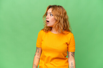Young caucasian woman isolated on green screen chroma key background doing surprise gesture while looking to the side