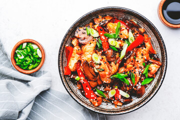 Stir fry with turkey fillet, red paprika, mushrooms, green chives and sesame seeds in bowl Asian cuisine dish. White kitchen table background, top view