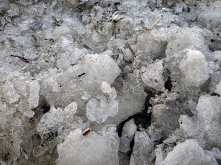 Lumps of melted snow on a spring day. The surface of dirty snow in the rays of the sun, top view. Snow and mud in the sun, close-up.
