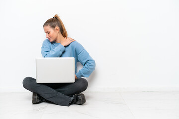 Young woman with a laptop sitting on the floor suffering from pain in shoulder for having made an effort