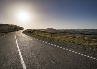 Asphalt road on a mountain hill in the light of the evening sun, track among the mountain ranges