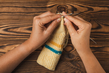 Knitting socks. work in progress. Woolen yarn in the hands of a woman on a brown texture wood....