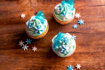 Homemade cupcake of blue color placed on wooden desk. Winter and christmas theme, snowflakes on cream with blue ice. Fresh and home baked sweet.