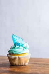 Homemade cupcake of blue color placed on wooden desk. Winter and christmas theme, snowflakes on cream with blue ice. Fresh and home baked sweet.