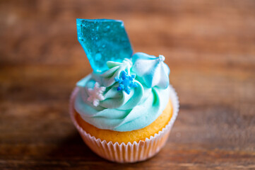 Homemade cupcake of blue color placed on wooden desk. Winter and christmas theme, snowflakes on...