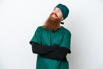 Surgeon redhead man in green uniform isolated on white background looking up while smiling