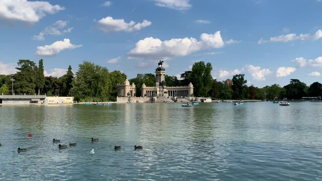 Ducks are swimming in a big pond, lake at the Buen Retiro Park (Parque del Buen Retiro). Alfonso XII monument and tiny boats in the background. This park is a popular recreation place. Madrid, Spain