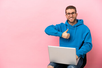 Young man sitting on a chair with laptop giving a thumbs up gesture