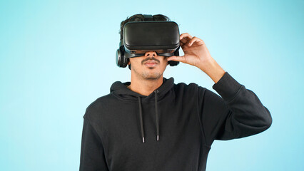 Young Indian Asian man using VR headset, glasses or goggles, isolated over blue colour indoor studio background, future, gadgets, technology, education online, studying, video game concept