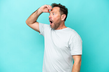 Fototapeta na wymiar Middle age caucasian man isolated on blue background doing surprise gesture while looking to the side