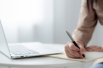 Closeup hands young asian woman writing on notebook for planning working and using laptop computer...
