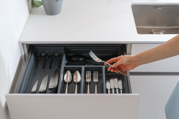 woman taking fork from drawer with cutlery at kitchen