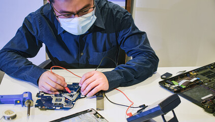 young man wearing glasses who is a technician computer technician A laptop motherboard repairman is...