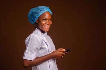 Smiling Nigerian female medic holding a smartphone isolated on a brown background