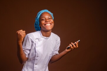 Excited Nigerian female medic holding a smartphone isolated on a brown background