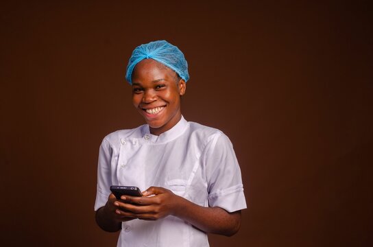 Smiling Nigerian female medic holding a smartphone isolated on a brown background