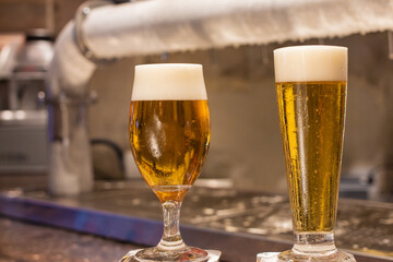 two glasses of cold and creamy beer on the counter of a lighted bar
