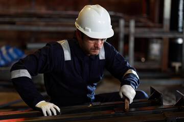 Skilled industrial worker finishes polishing rusty piece of metal on a table and rubs the dust with his hand. Interior of heavy industry machine building plant.