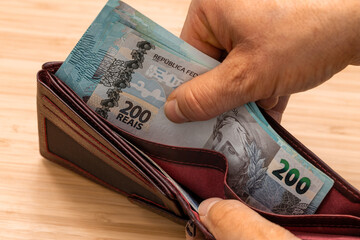 Hand taking money out of wallet, Brazil Real banknotes, high BRL values, concept, rising prices,...