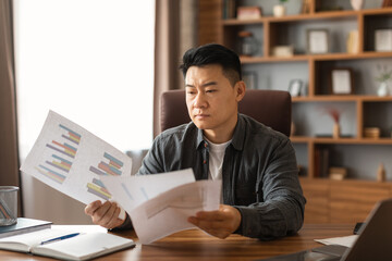 Busy serious concentrated middle aged asian man reads documents, think about project in home office...