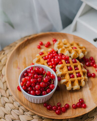 Belgian waffles with red currants on a wooden plate on a white background