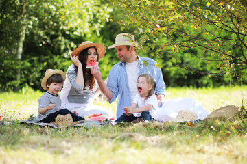 Happy family with children having picnic in park, parents with kids sitting on garden grass and eating watermelon outdoors