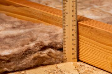 Measuring fiberglass insulation in attic of house with ruler. Home energy savings, heating and...