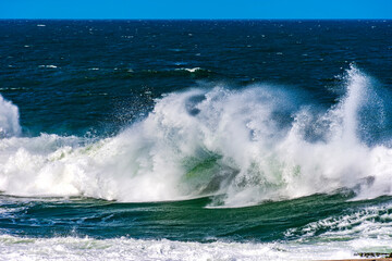 Fototapeta premium Beautiful and strong atlantic sea waves with water drops and foam splashing in the air on a blue sunny day