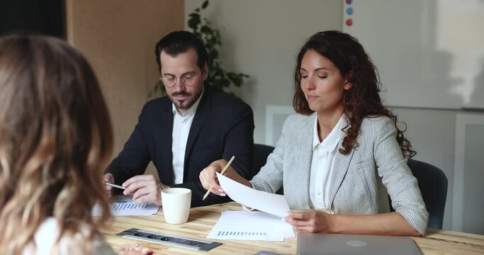 Attractive Hispanic businesswoman talking, take part in group meeting sit at desk, share sales statistics, work result to business partners, makes speech participate in seminar with diverse teammates