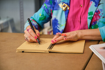 Unrecognizable dressmaker with colorfull clothes drawing new layout in a sewing workshop.