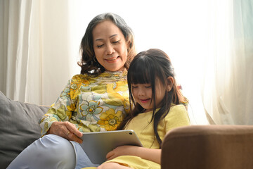 E-learning with diversity age people at home concept, Granny teaching a little girl using digital tablet for promote learning.