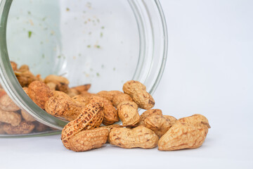 Peanuts coming out of a glass jar. Isolated on white background