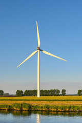 Tall wind turbine in a farm field in evening dusk ight. No people.