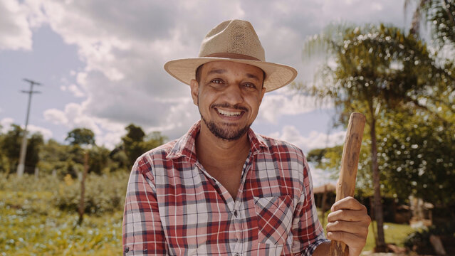 Portrait of young man in the casual shirt holding his hoe in the farm. Farm tool. Latin man.
