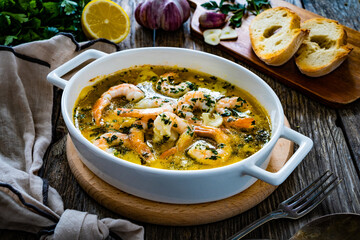 Roast prawns in butter sauce with lemon, garlic and parsley on wooden table
