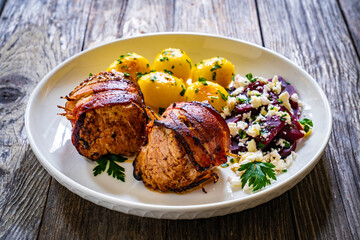 Medium well done pork loin wrapped in bacon with fried potatoes and feta cheese on beets on wooden table
