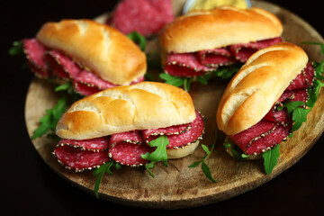 Appetizing salami sandwiches with arugula and mustard on a wooden board.