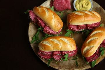 Appetizing salami sandwiches with arugula and mustard on a wooden board.