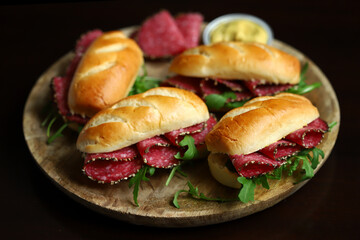 Appetizing salami sandwiches with arugula and mustard on a wooden board.