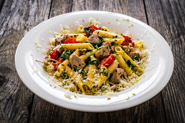 Roasted chicken nuggets, cherry tomatoes, spinach and penne served on wooden table
