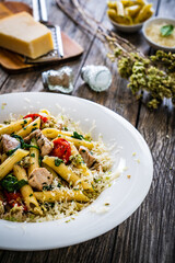 Roasted chicken nuggets, cherry tomatoes, spinach and penne served on wooden table
