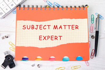 Subject matter expert a word on a sheet from a notebook lying on a notebook next to office supplies, a calculator, a USB flash drive, a pen, paper clips