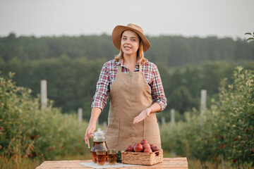 Obraz premium Happy smiling female farmer worker with tasty juice and fresh ripe apples in orchard garden during autumn harvest. Harvesting time