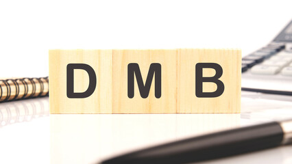 DMB text on wooden cubes on the table next to a calculator, pen, notepad