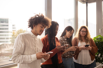 Young people in the office, using phone in front of the window