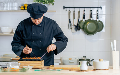 Portrait handsome professional Japanese male chef wearing black uniform, hat, cooking, making takoyaki street food, smiling with confidence, standing in kitchen. Restaurant, Hotel Concept.